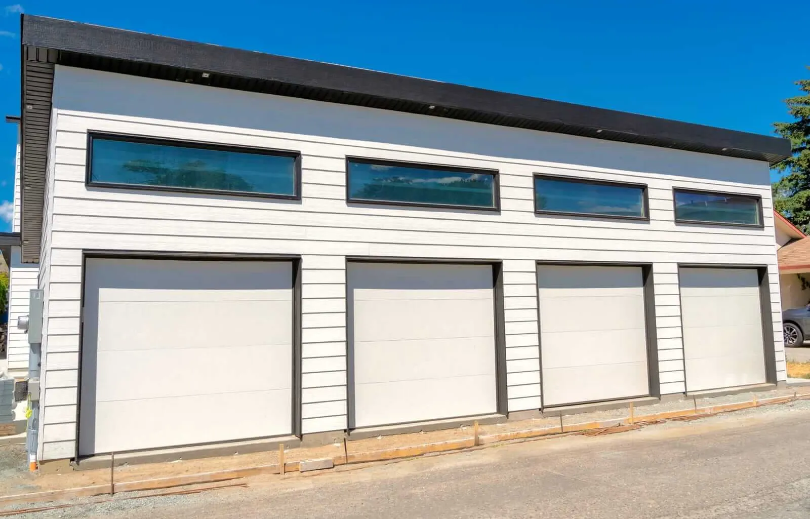 A modern white building with three garage doors and three narrow rectangular windows above them, set against a clear blue sky.